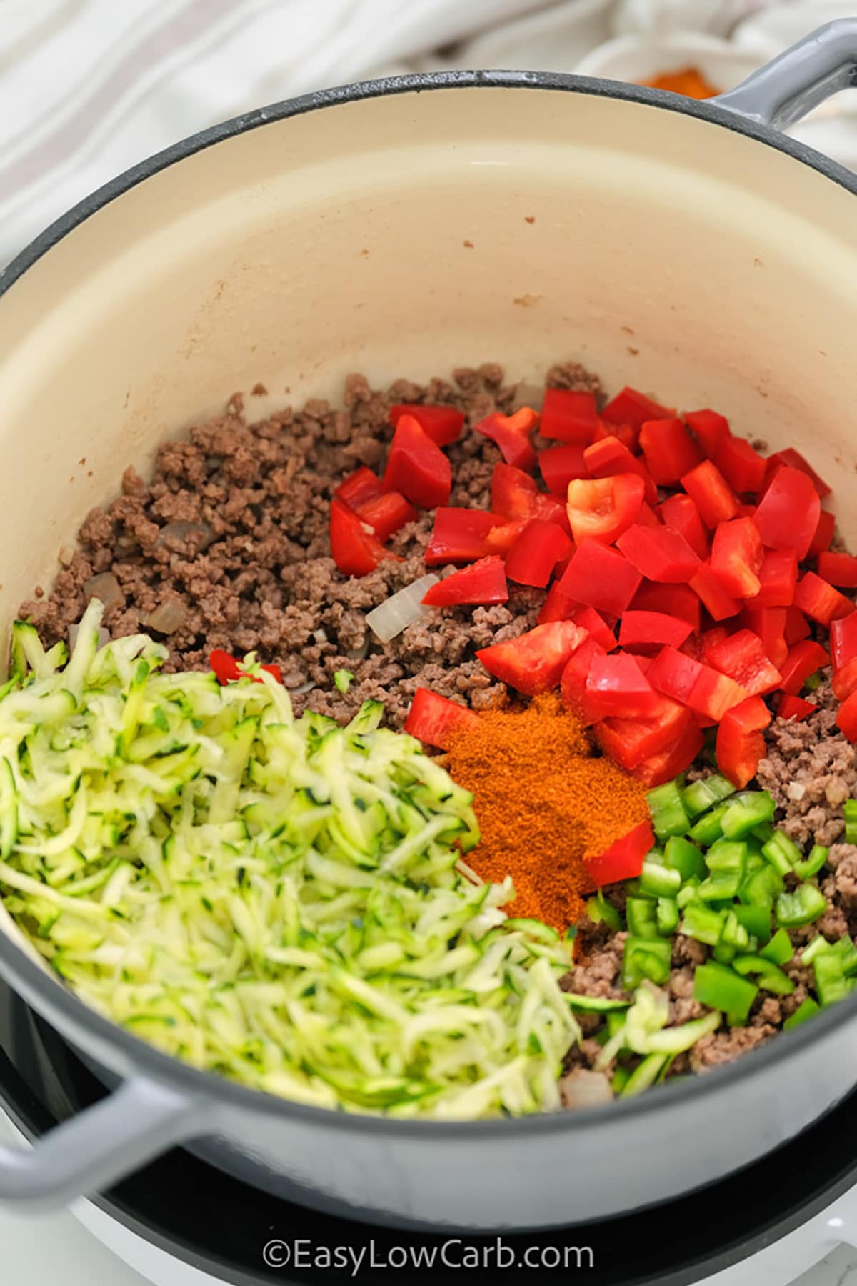 adding vegetables to cooked beef to make Keto Chili Recipe