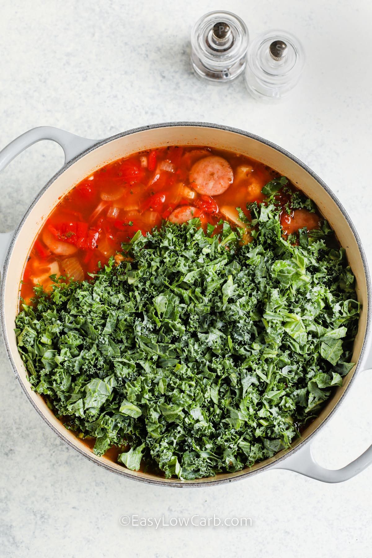 kale being added to sausage kale soup in a pot