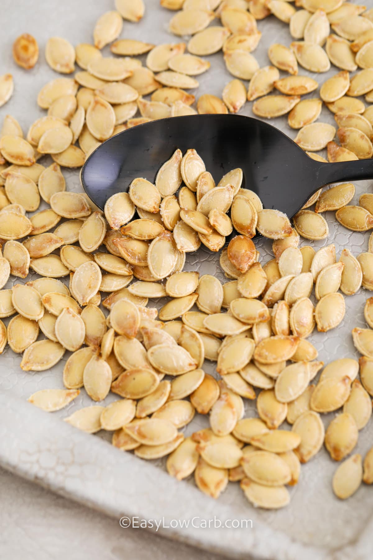 scooping pumpkin seeds with a spoon from a baking sheet