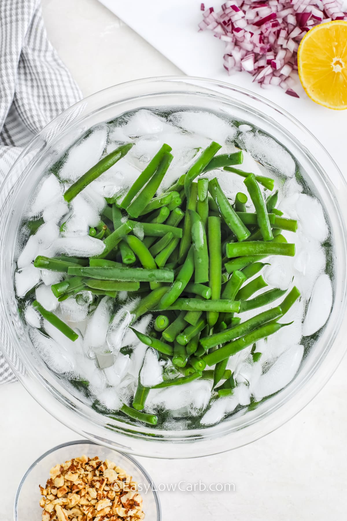 green beans in an ice bath with remaining green bean salad ingredients around it.