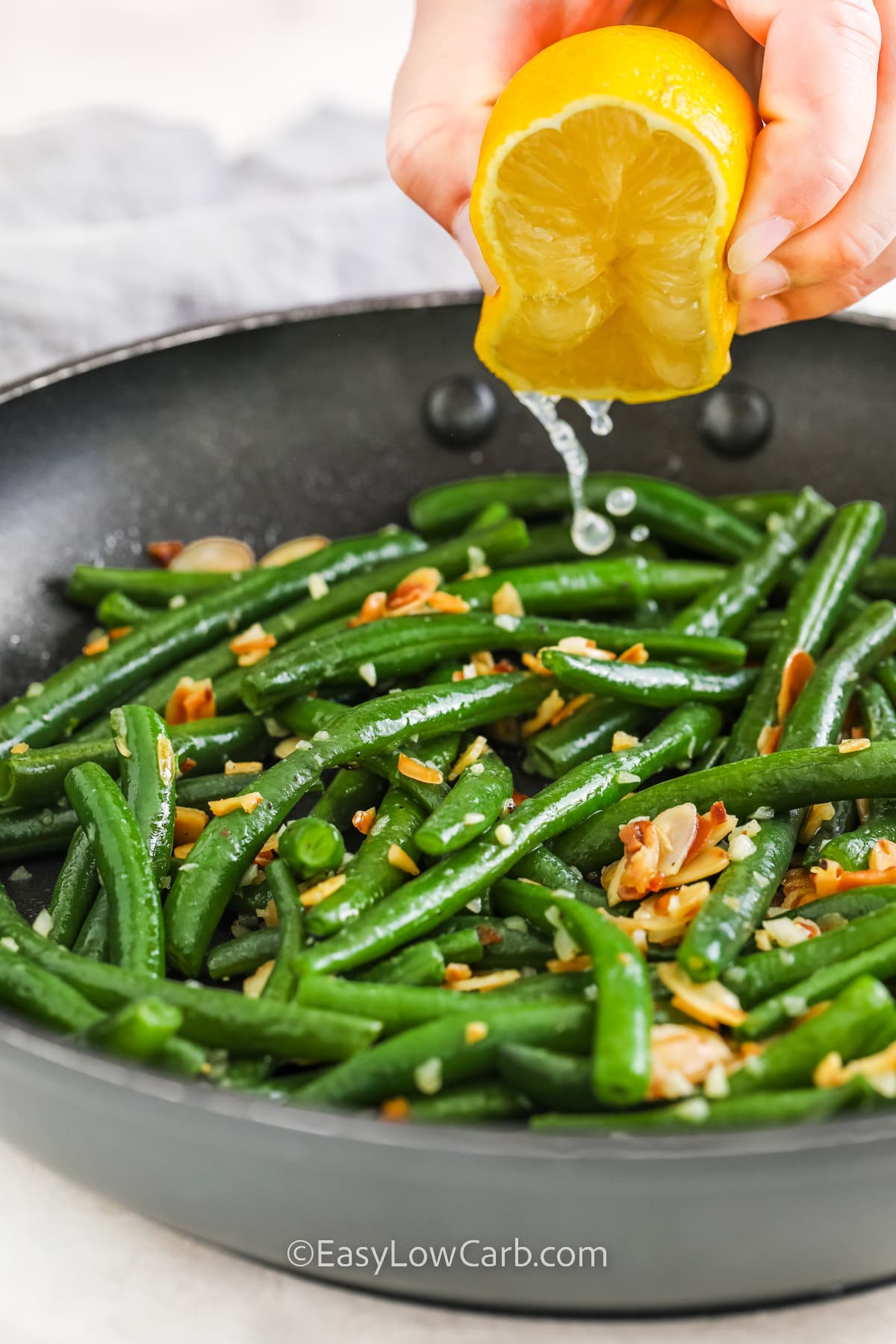Lemon being squeezed onto prepared green beans almondine in a frying pan