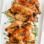 Two roasted Cornish hens on a serving dish with thyme