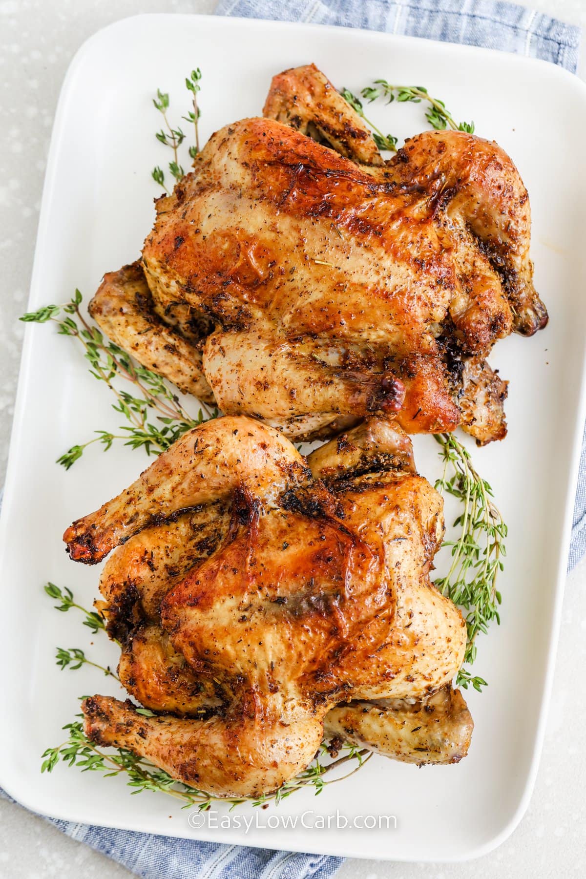 Two roasted Cornish hens on a serving dish with thyme