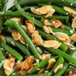 A serving bowl of green beans almondine with text