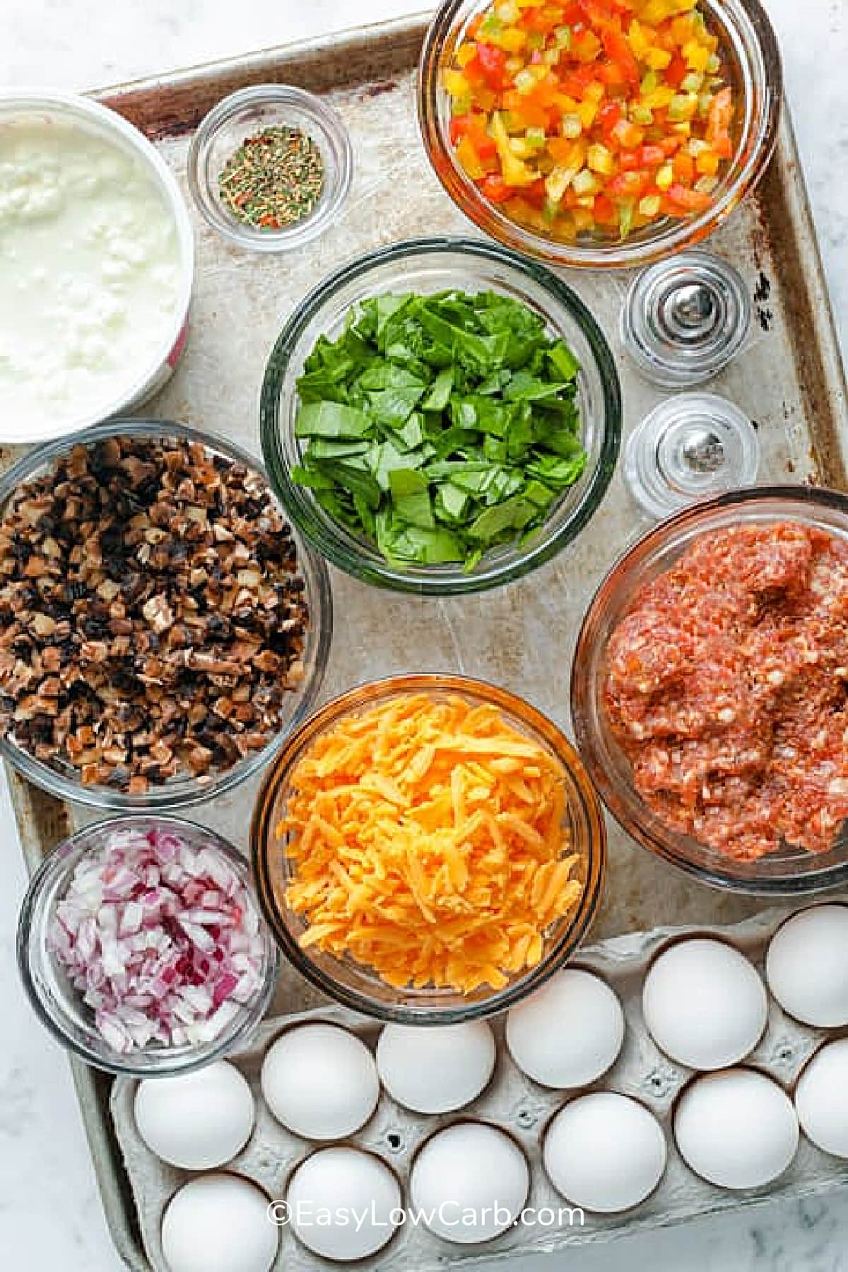 ingredients to make sausage egg casserole including cottage cheese, cheddar, spinach, onions, bell pepper, Italian seasoning, sausage, and eggs