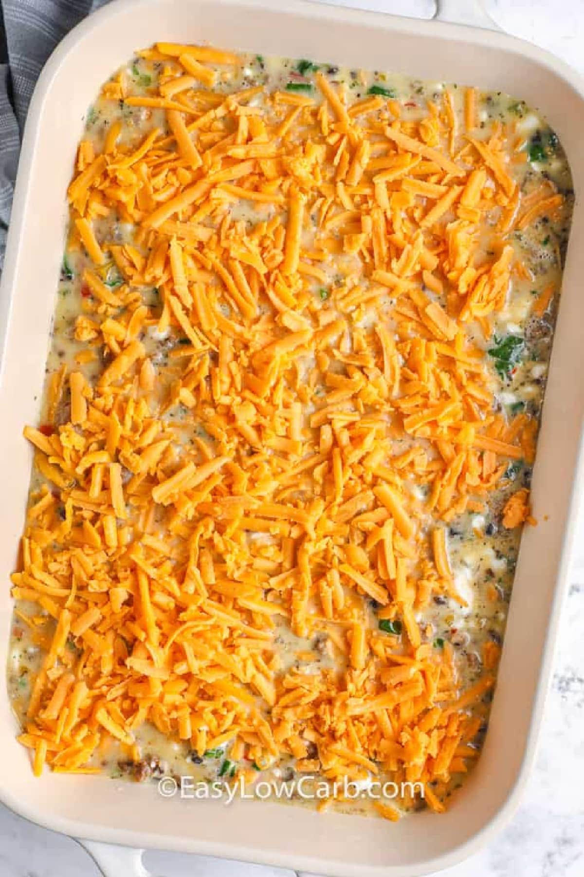 Sausage Egg Casserole, with cheddar sprinkled on top, in a baking dish before baked