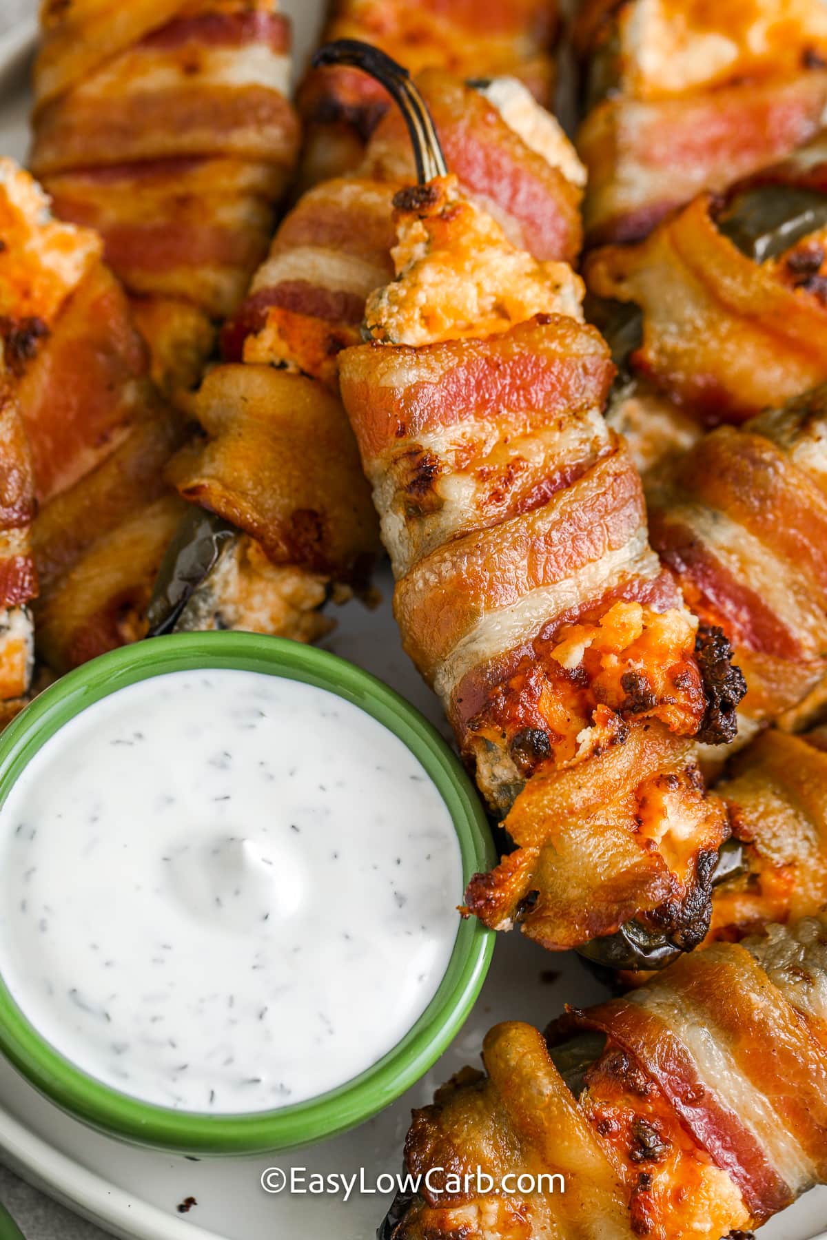 bacon wrapped jalapenos on a plate with a bowl of dip on the side