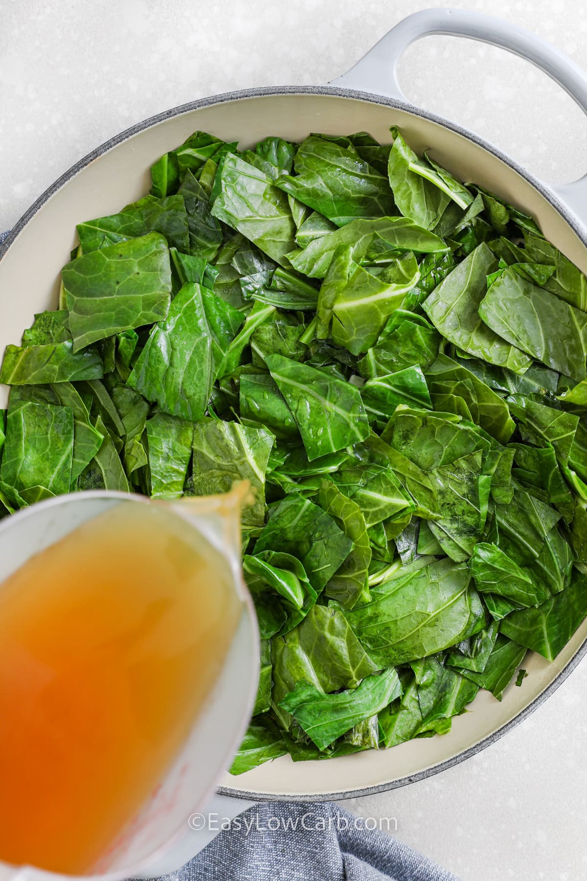 collard greens in a pan with broth being poured in