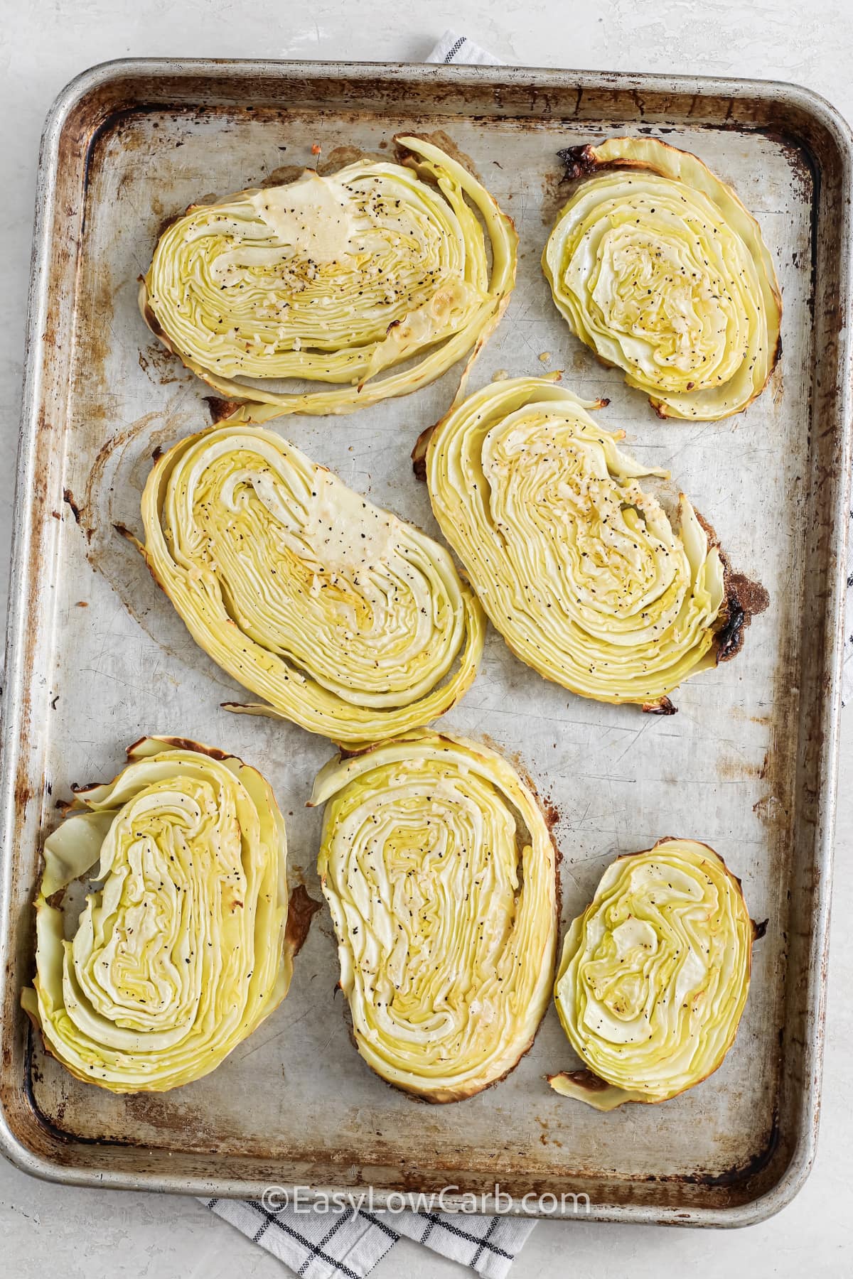 Cabbage steaks are the perfect way to enjoy roasted cabbage in a new form. Seasoned with garlic butter and baked until golden, each slice delivers savory flavor and tender texture. This easy low-carb recipe makes a satisfying vegetable side dish for family meals or holiday tables. Serve these oven-roasted cabbage slices with beef, chicken, or pork for a balanced plate that feels hearty and nourishing. It is a simple recipe with big flavor payoff. #easylowcarb Roasted Cabbage Steaks on a baking tray