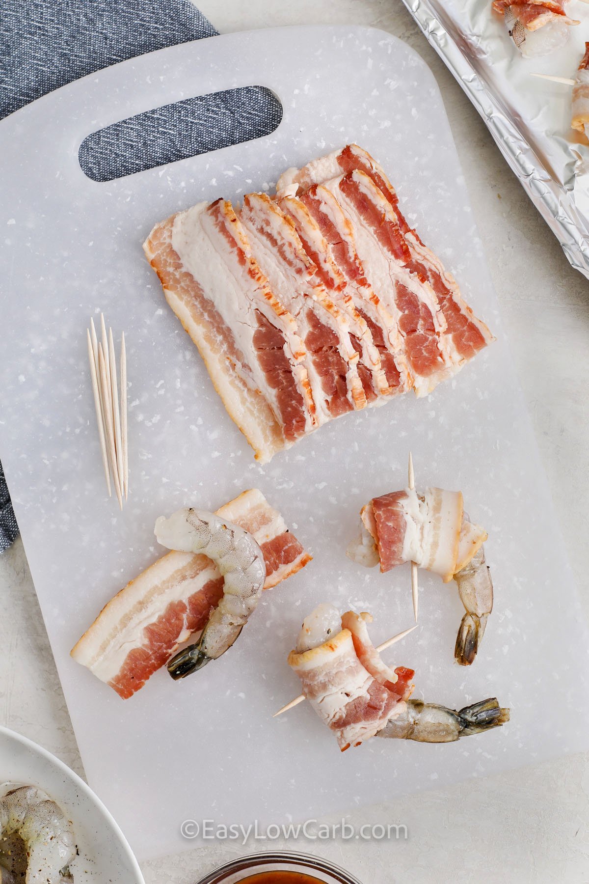 bacon being wrapped around shrimp on a cutting board