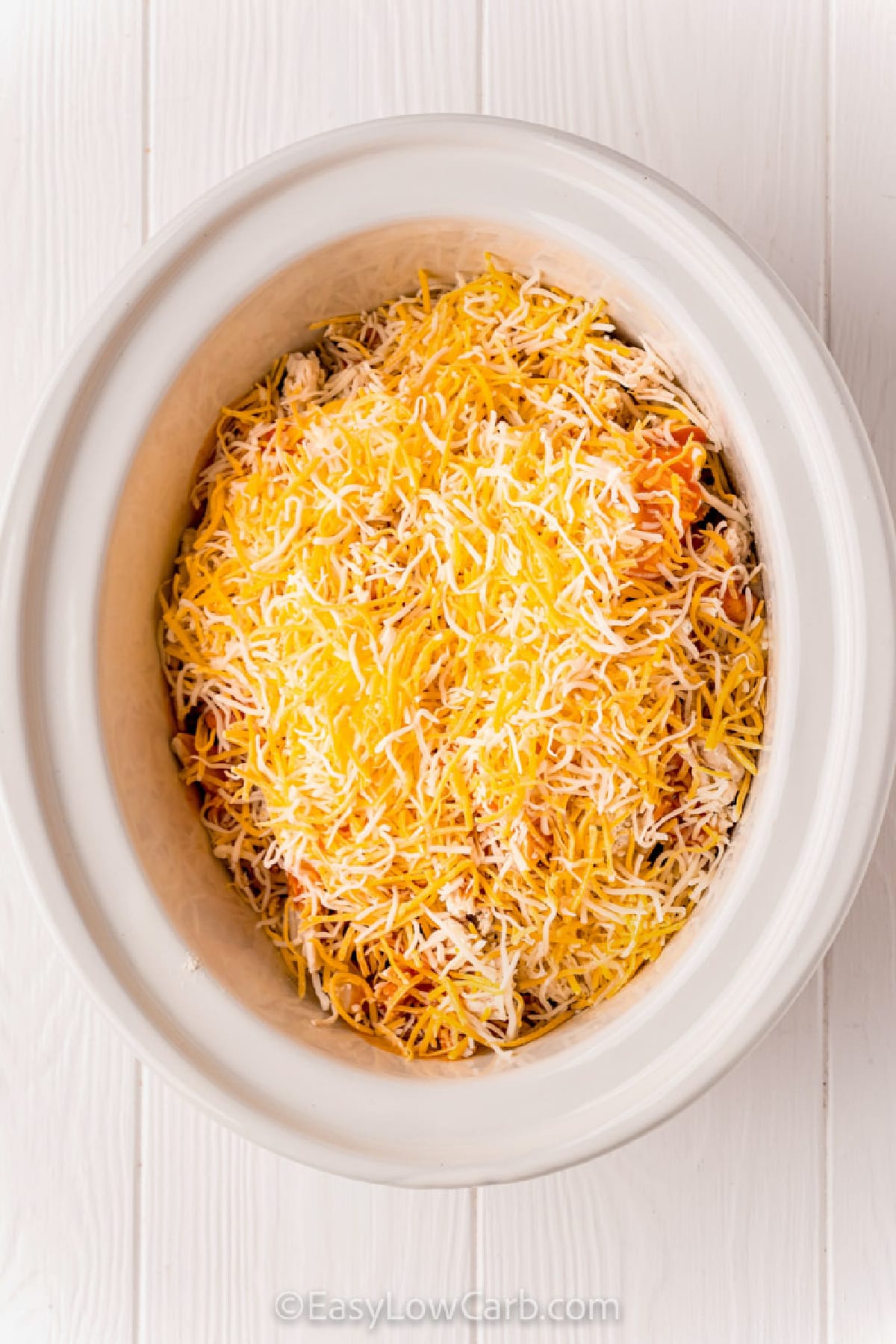 shredded cheese added to the other ingredients in a crock pot to make crock pot buffalo chicken dip recipe