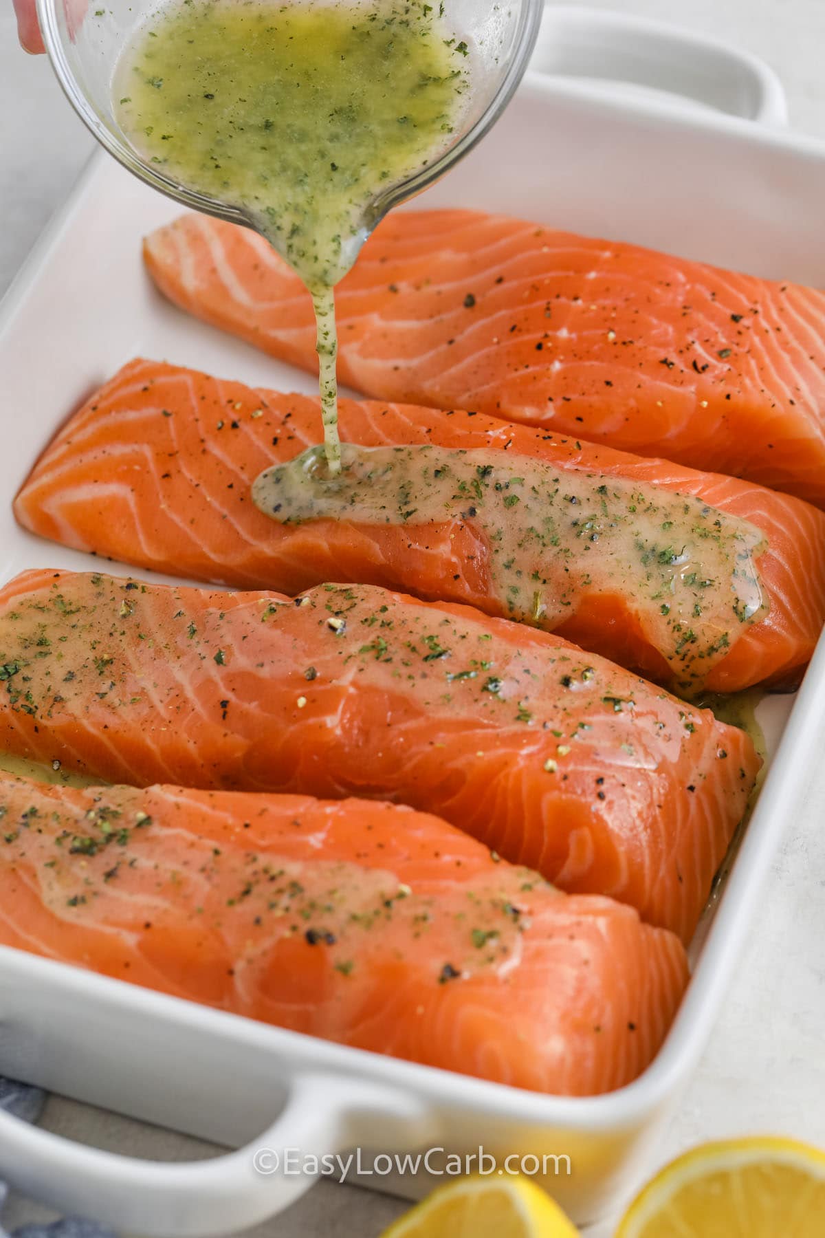 garlic butter being poured over salmon filets in a baking dish