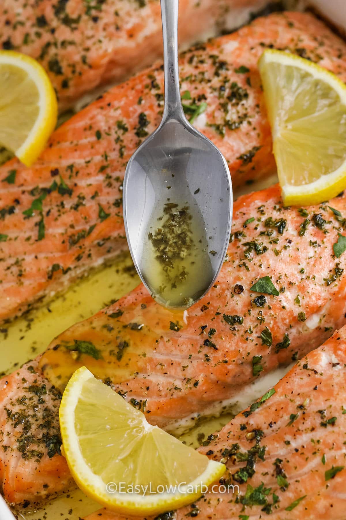garlic butter being spooned over cooked salmon filets with lemon slices