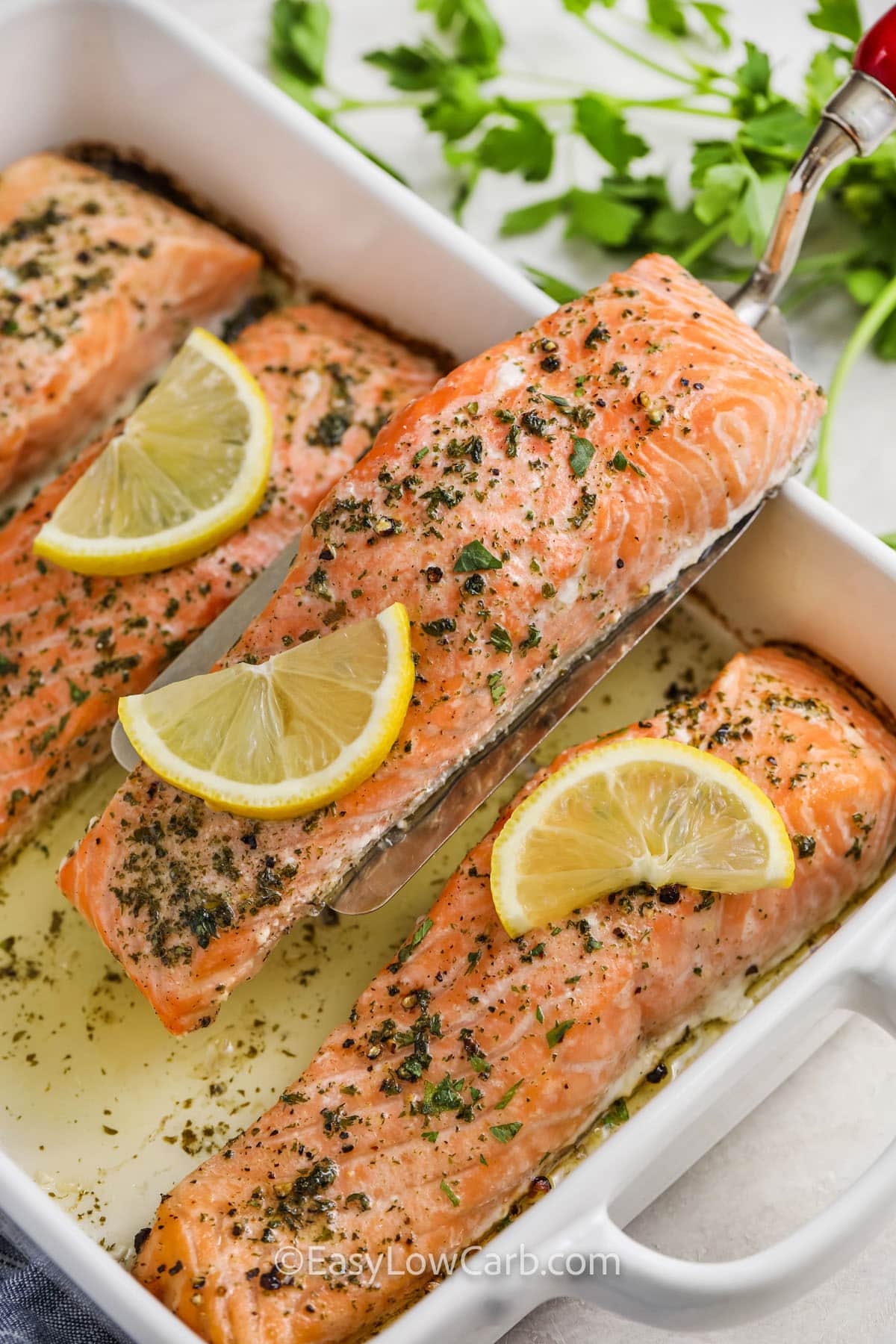 a garlic butter salmon filet being lifted out of the baking dish