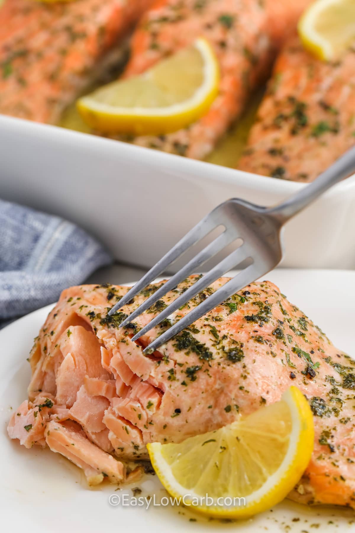 a fork flaking apart a garlic butter salmon filet with a lemon slice