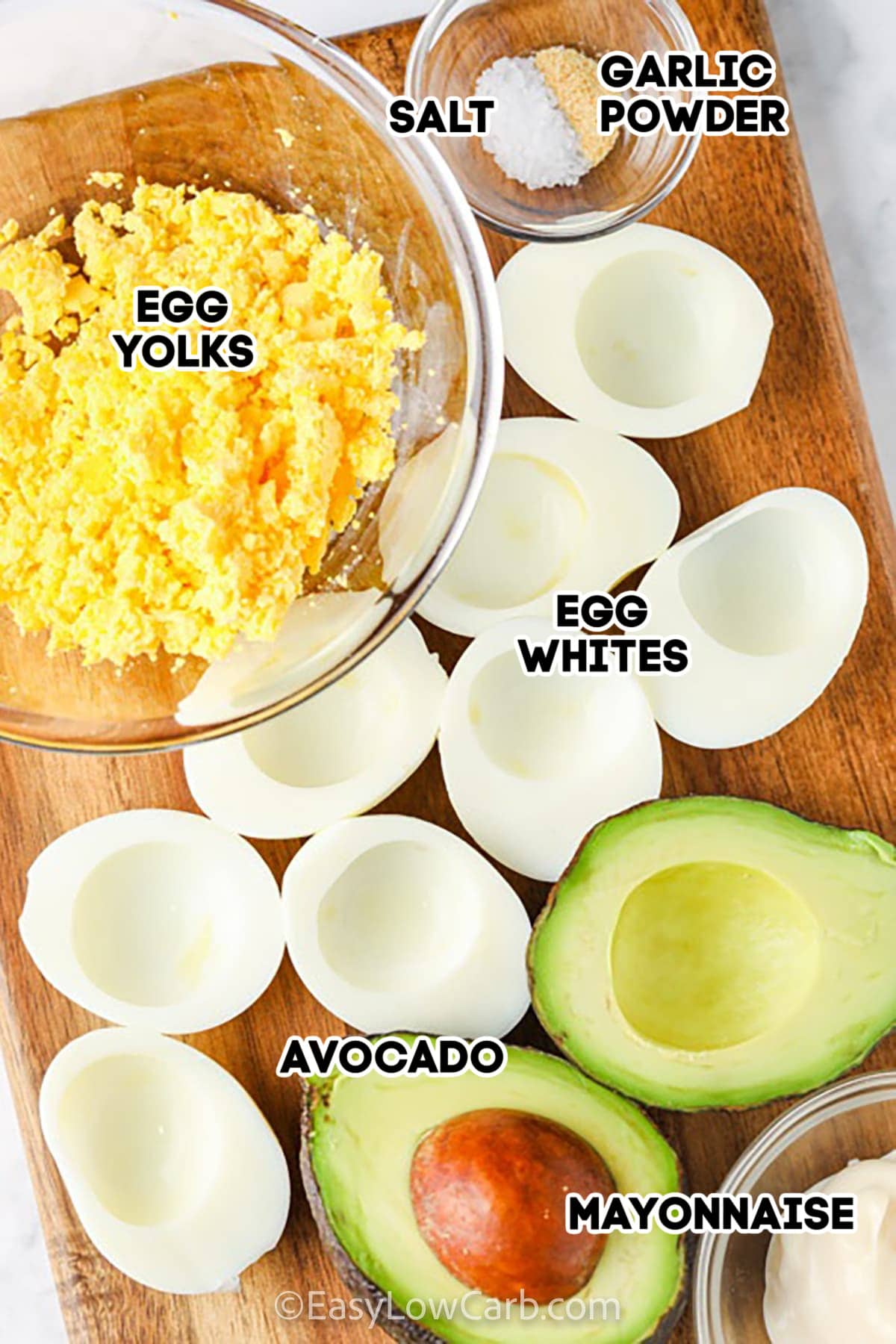 egg yolks, egg whites, avocado, mayonnaise, salt and garlic powder on a wooden board to make avocado deviled eggs
