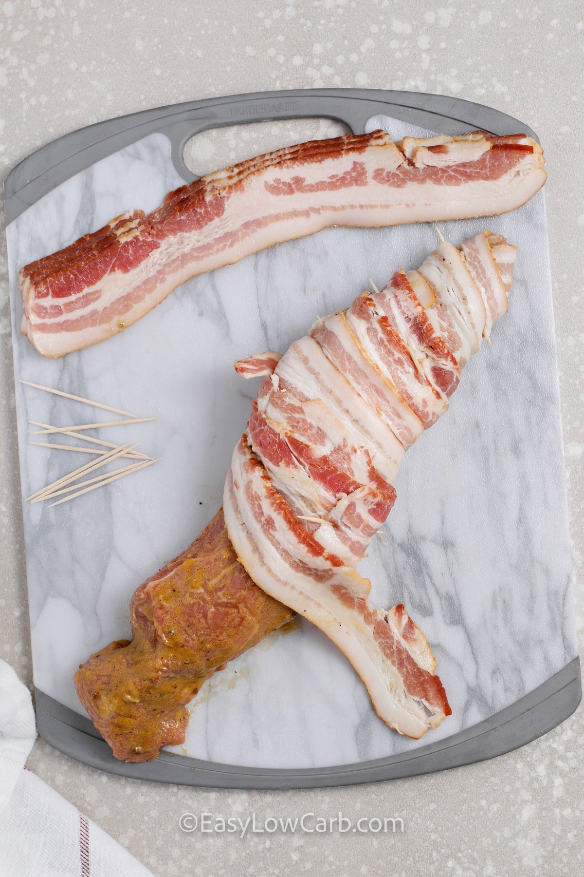 seasoned pork tenderloin being wrapped with bacon