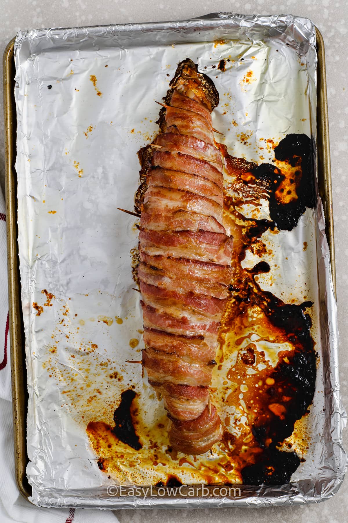 bacon wrapped pork tenderloin cooked on a baking sheet