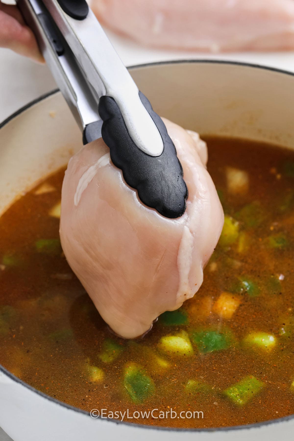 a chicken breast being added to a pot of chicken taco soup mixture
