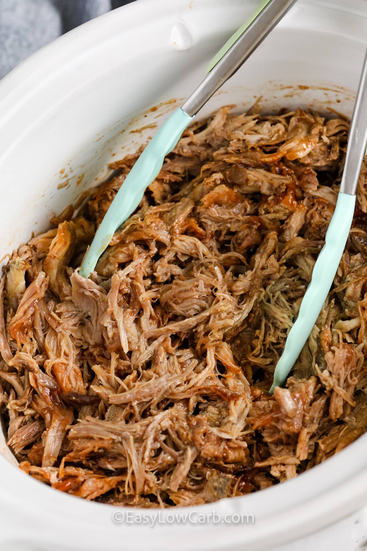 Shredded pulled pork in a crock pot with tongs