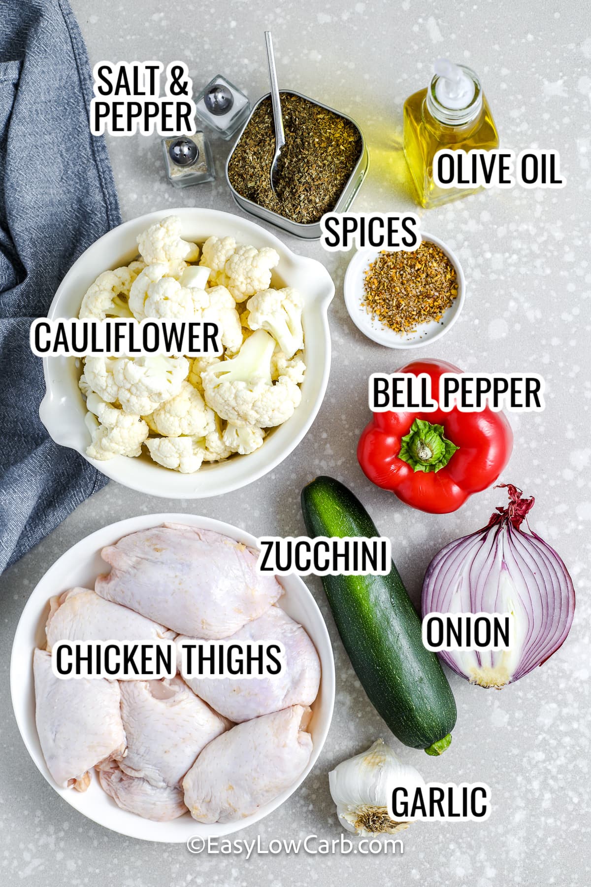 ingredients assembled to make sheet pan chicken and veggies including cauliflower, chicken thighs, zucchini, bell pepper, onion, and spices