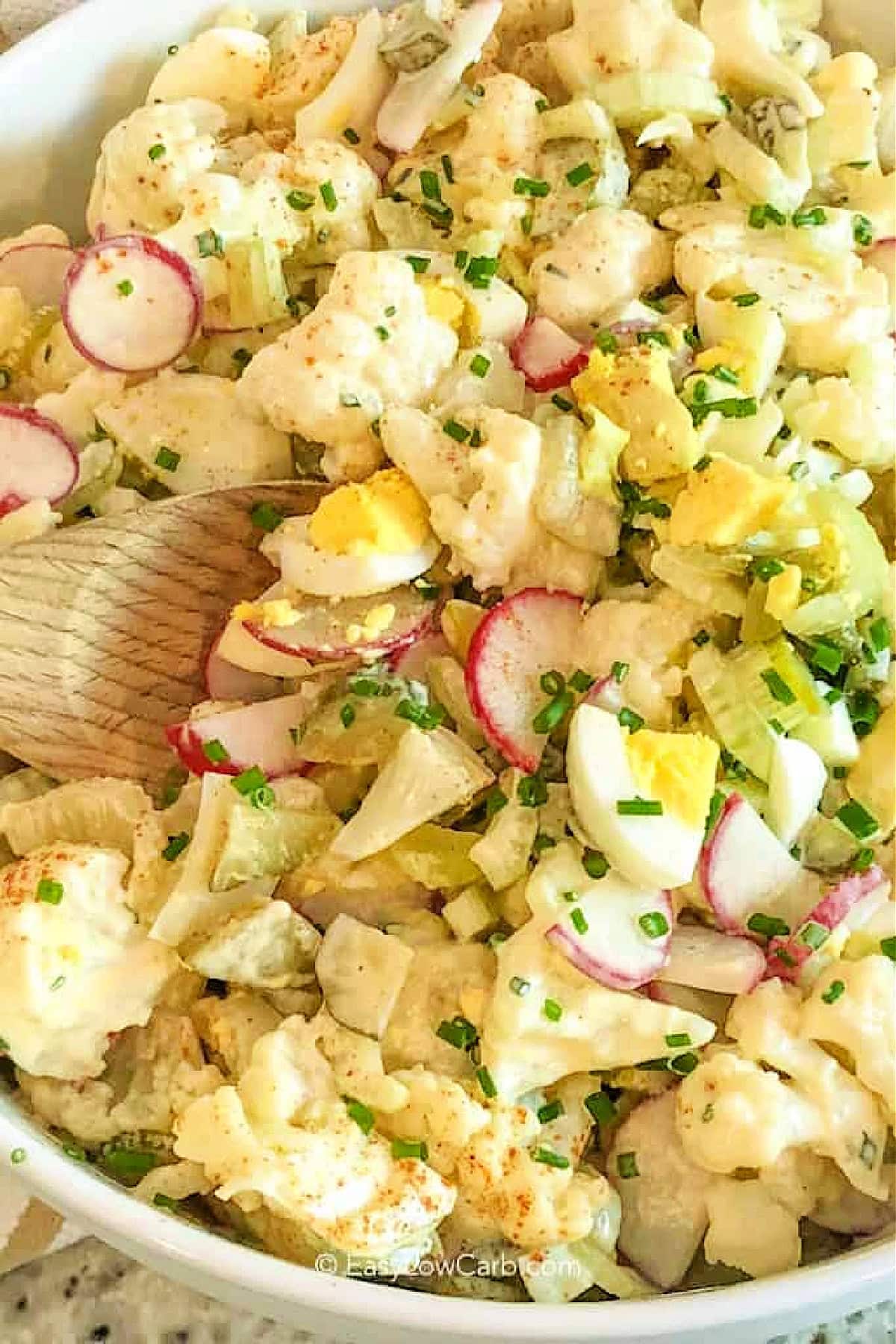 Cauliflower potato salad in a white bowl with a wooden spoon