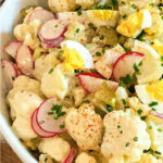 Cauliflower potato salad in a white bowl, garnished with sliced green onion