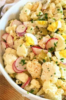 Cauliflower potato salad in a white bowl, garnished with sliced green onion