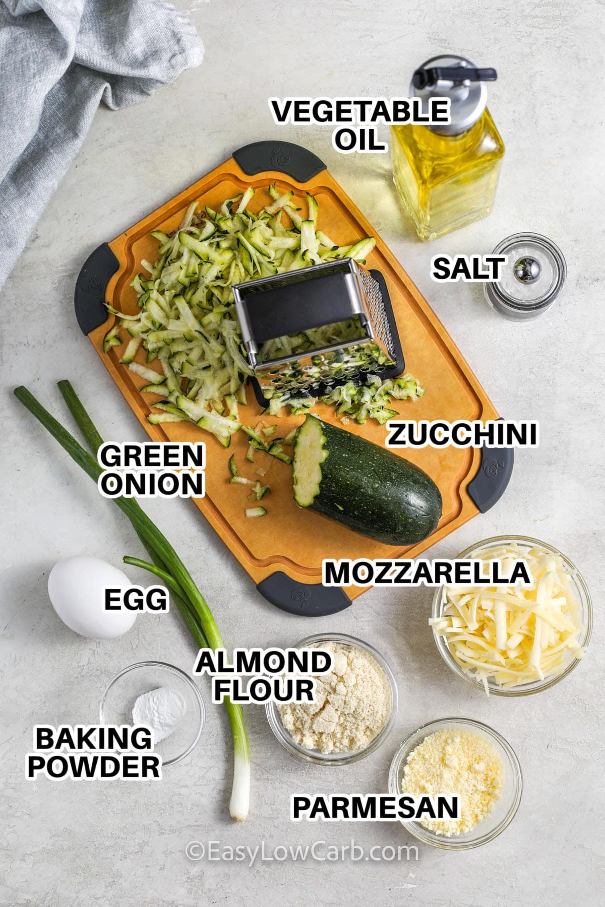 Ingredients to make zucchini fritters labeled: vegetable oil, salt, green onions, zucchini, mozzarella, egg, almond flour, mozzarella, parmesan, and baking powder.