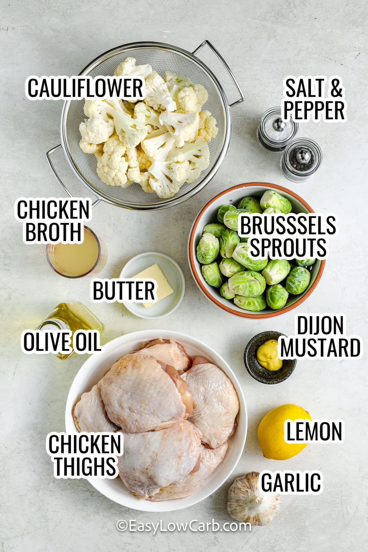 ingredients assembled to make braised chicken thighs, including chicken thighs, cauliflower, brussels sprouts, dijon mustard, broth, butter, lemon, and garlic