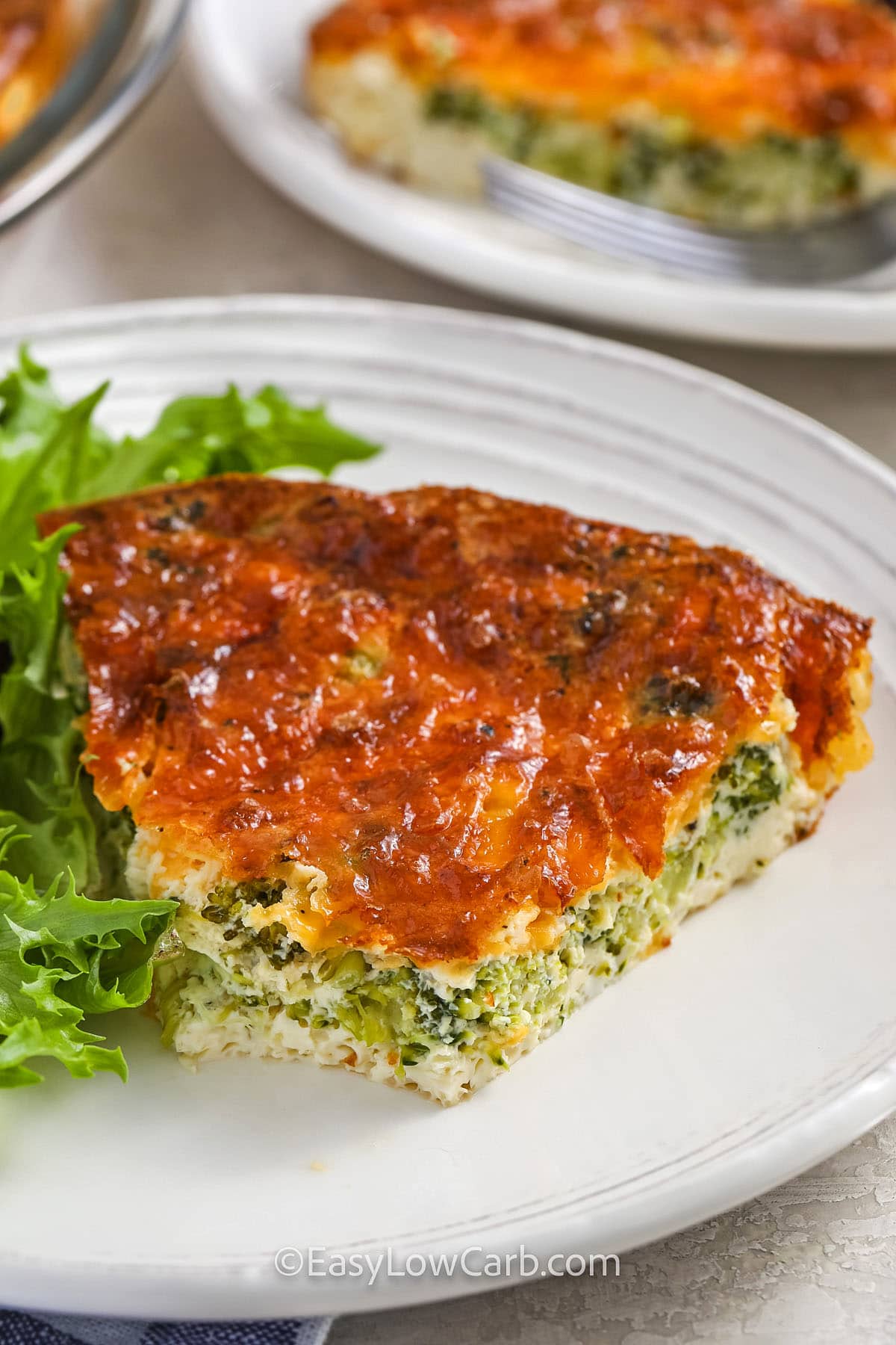 A slice of broccoli cheese quiche with a bite missing on a plate