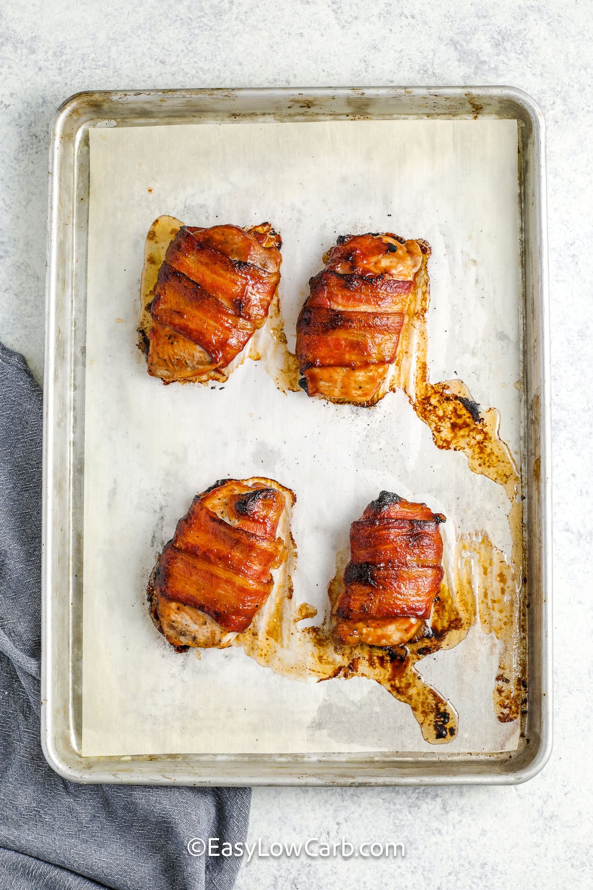 four bacon wrapped pork chops on a baking tray