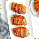 3 bacon wrapped pork chops on a serving plate