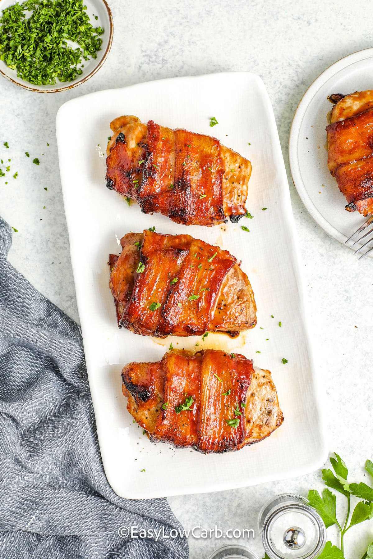 3 bacon wrapped pork chops on a serving plate