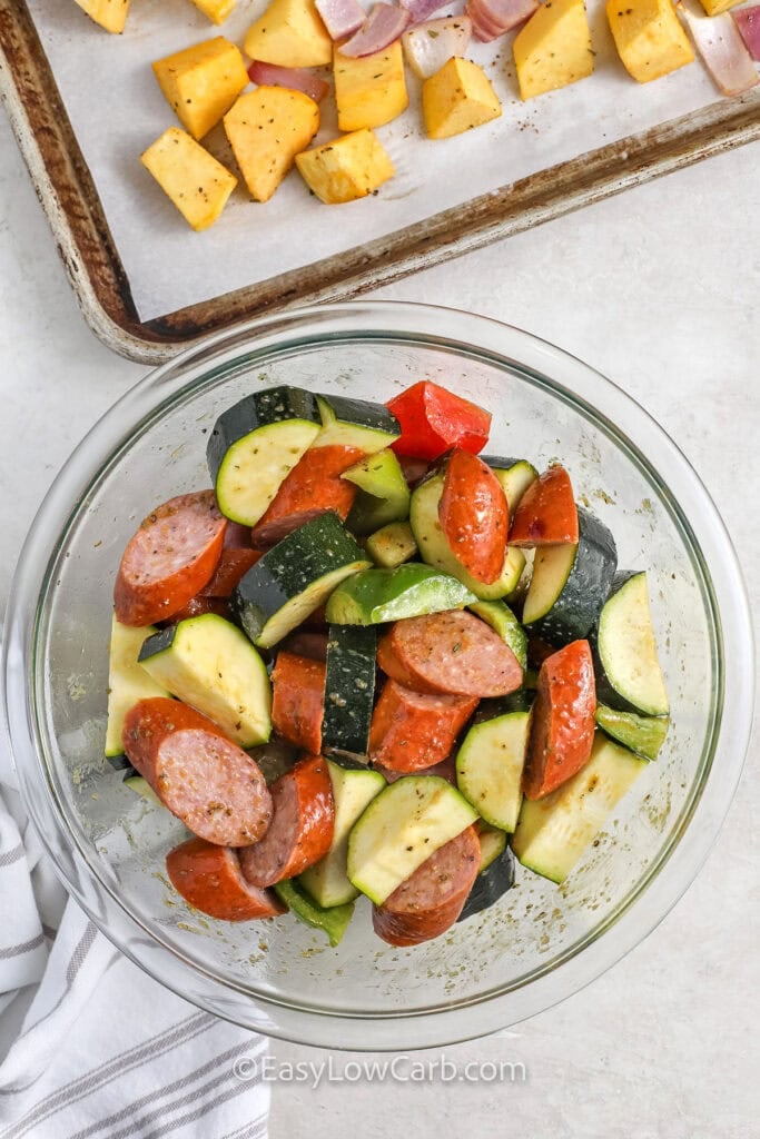 adding vegetables and sausage to bowl with seasonings to make Sheet Pan Sausage and Vegetables