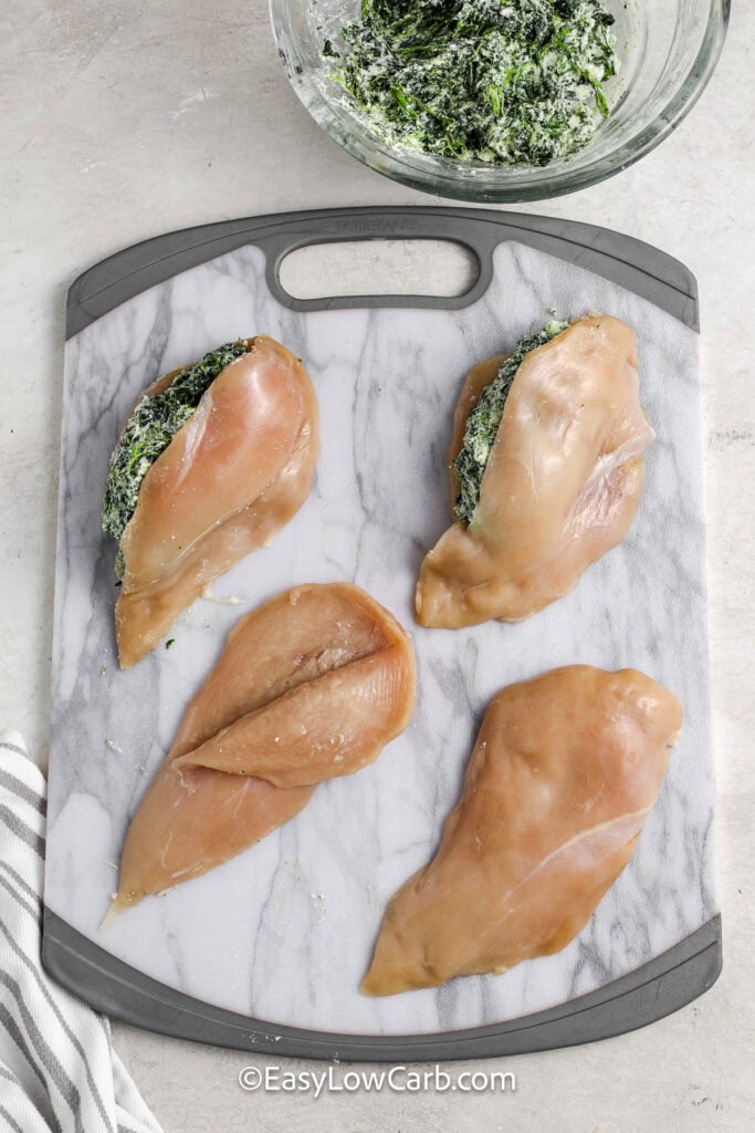 chicken breasts being stuffed with spinach filling on a cutting board