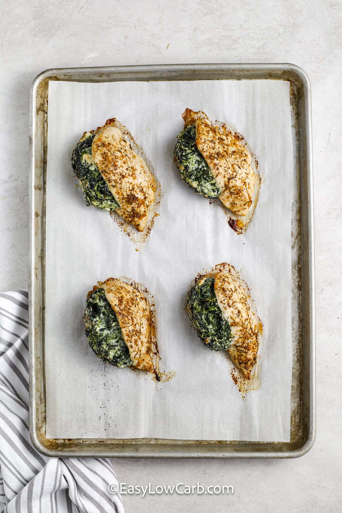 Spinach stuffed chicken breast is a simple dinner that looks impressive on the table. Tender chicken breasts are filled with creamy spinach and feta cheese, then seasoned with Cajun spices and baked until perfectly juicy. This baked chicken recipe is packed with flavor and makes a great low-carb dinner option. Pair it with steamed broccoli, cauliflower rice, or a fresh salad for an easy meal that is hearty and satisfying. #easylowcarb baked spinach stuffed chicken breasts on a baking tray