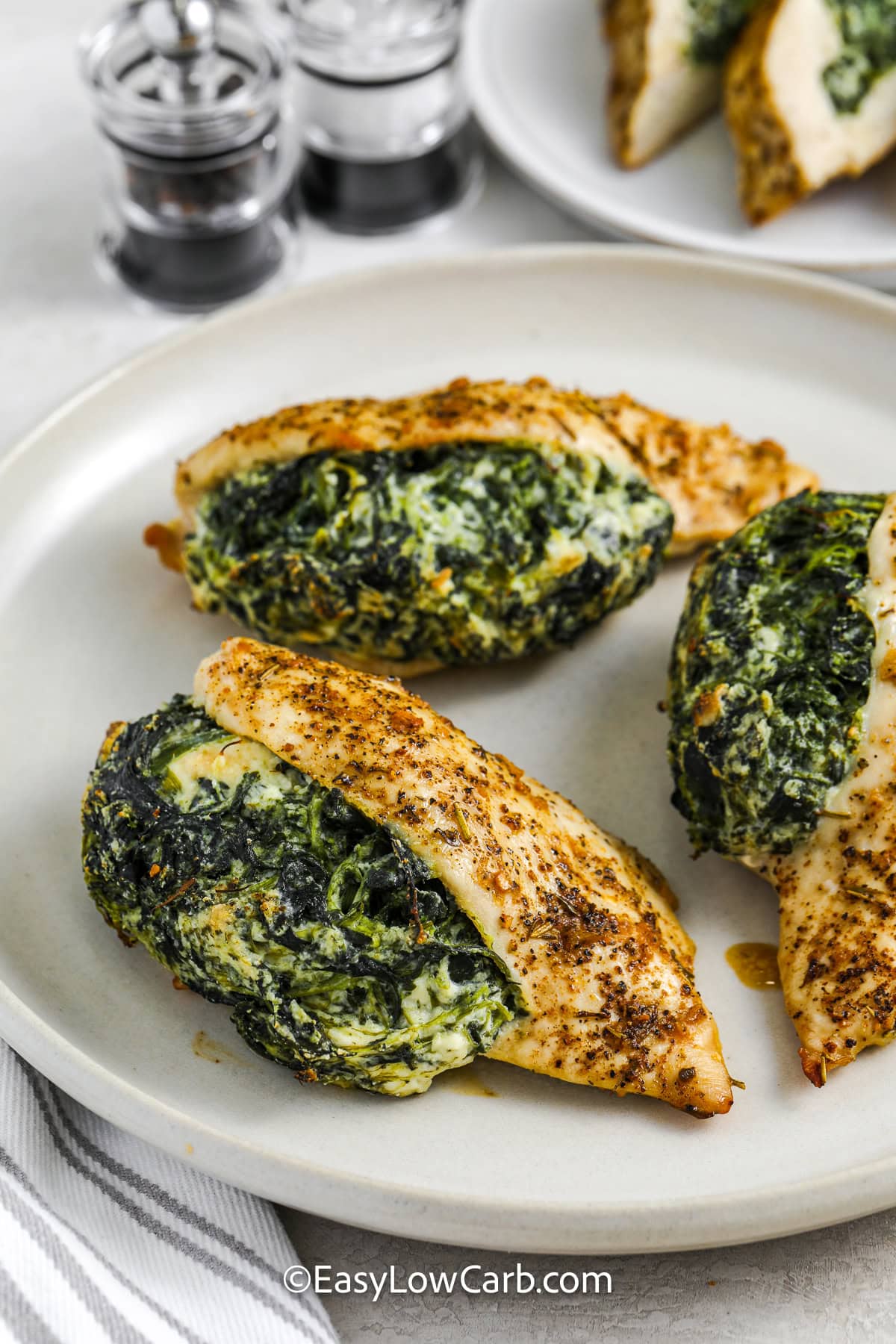 Spinach stuffed chicken breast is a flavorful baked chicken recipe that is perfect for dinner any night of the week. Each chicken breast is filled with a creamy spinach and feta mixture and seasoned with warm Cajun spices. The result is juicy chicken with plenty of savory flavor in every bite. It is a great low carb dinner idea served with roasted vegetables or a crisp side salad. #easylowcarb spinach stuffed chicken breasts on a plate