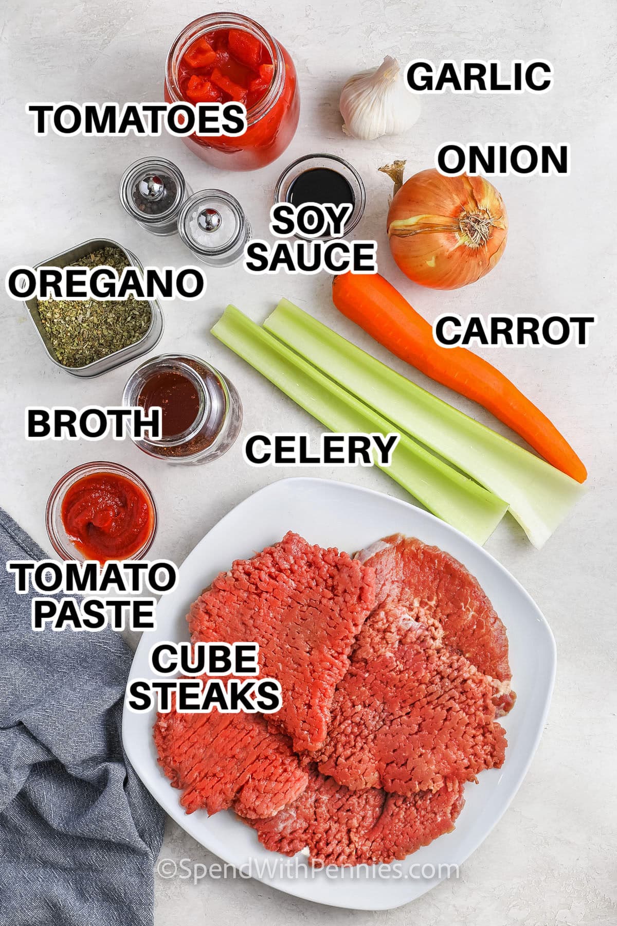 Ingredients to make slow cooker cube steak labeled: tomatoes, garlic, soy sauce, onion, carrot, celery, broth, oregano, tomato paste, cube steaks