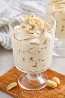 two cups of peanut butter mousse in dessert cups with peanuts and a cutting board