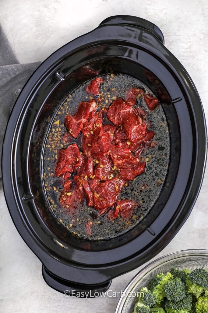 Adding beef strips to the sauce in a crock pot to make slow cooker beef and broccoli.