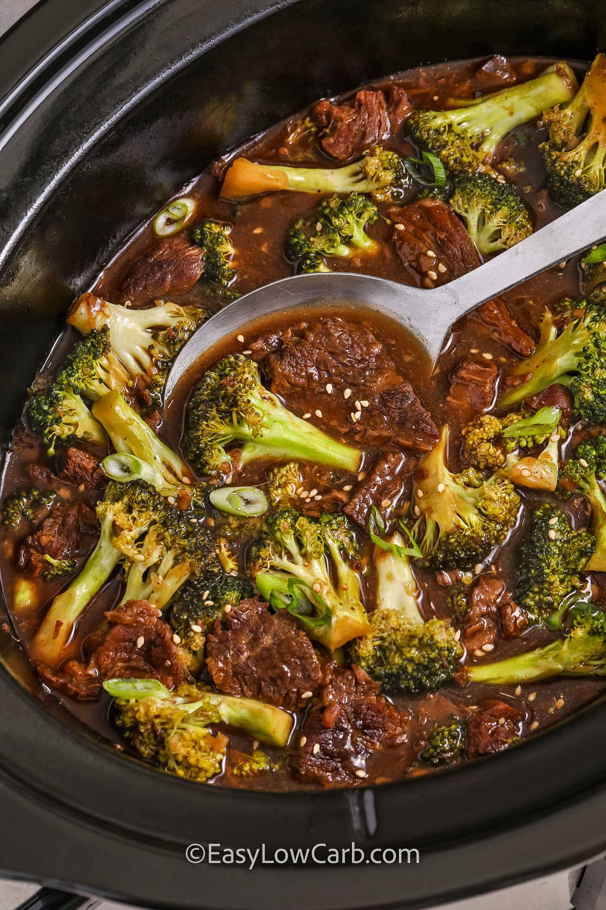 A pot of slow cooker beef and broccoli with a spoon scooping out a portion.