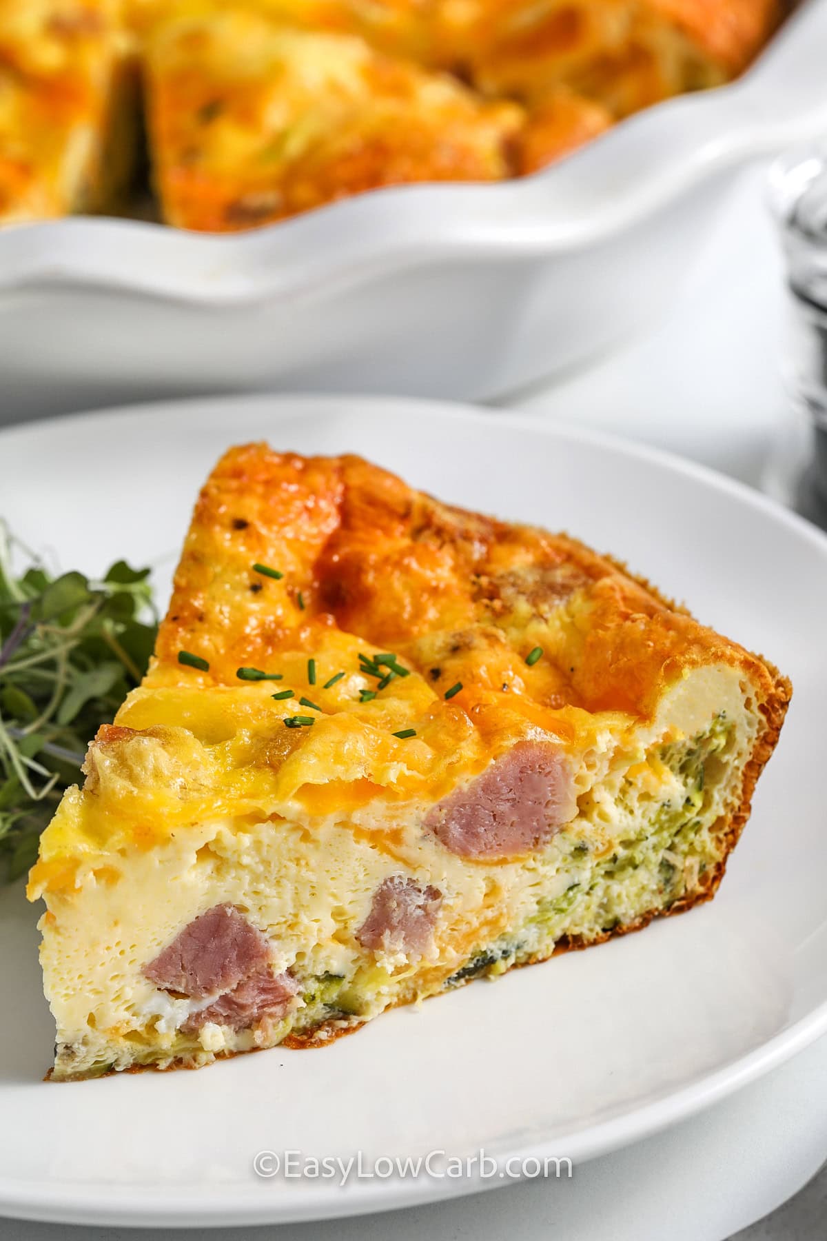 Crustless ham and cheese quiche is a delicious low carb breakfast idea when you want something warm, filling, and easy to reheat. Ham, cheddar, and zucchini are layered in a pie plate, then covered with a seasoned egg mixture and baked until set. This is the kind of simple egg bake busy home cooks will use again and again. #easylowcarb close up of a piece of Crustless Ham and Cheese Quiche