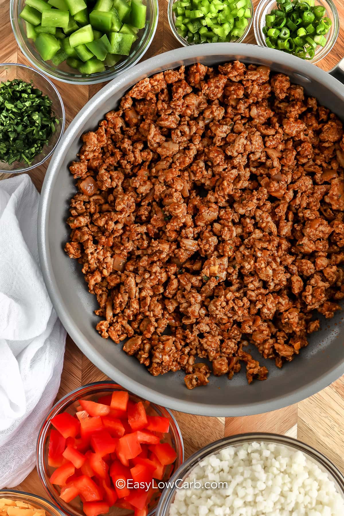 ingredients to make Cheesy Taco Skillet, including ground beef, onions, jalapenos, green and red bell peppers, cilantro, cauliflower rice, and cheese.