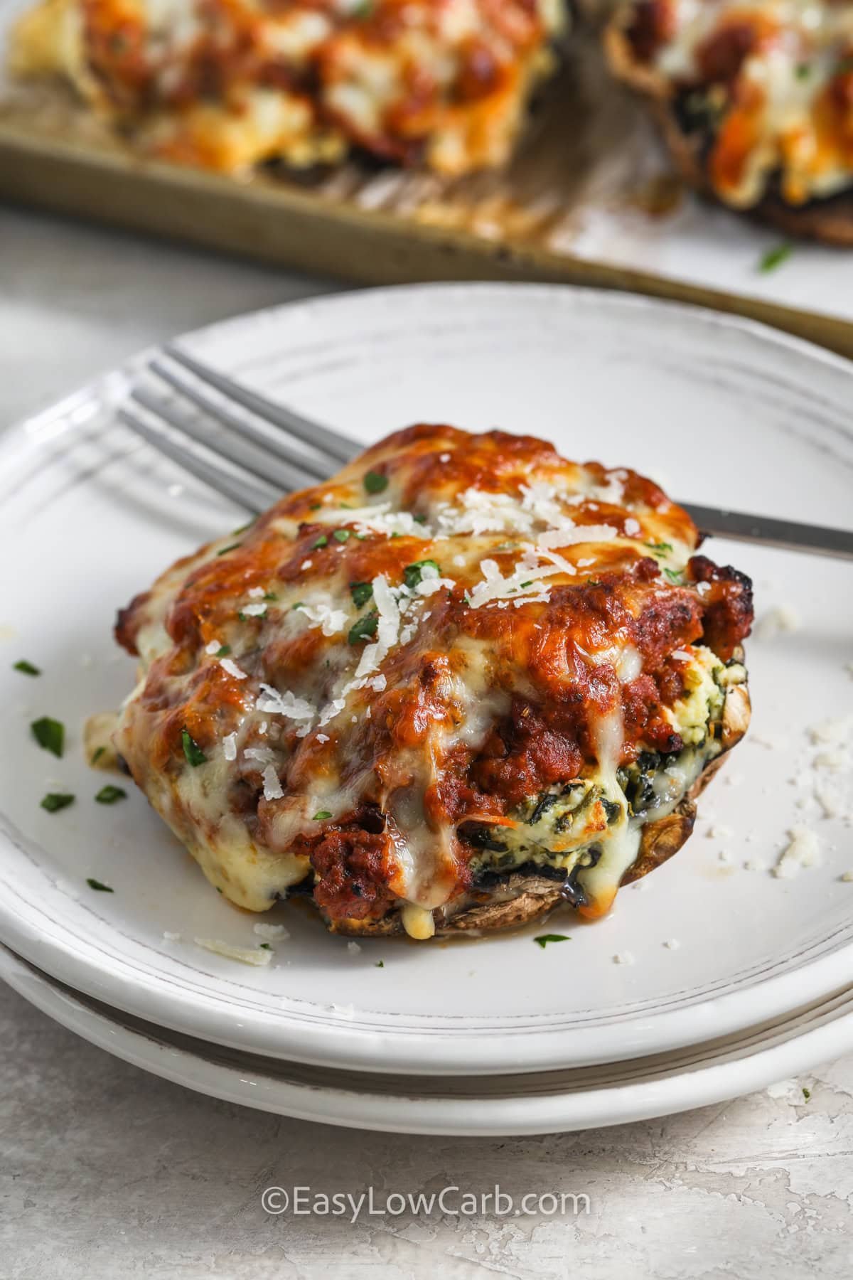 These lasagna stuffed mushrooms are a delicious way to enjoy classic lasagna flavors without the extra carbs! Each mushroom is packed with a creamy cheese and spinach filling, layered with a rich meat sauce, and topped with golden, melty cheese. They bake up juicy, flavorful, and satisfying, making them perfect for an easy dinner or meal prep. A low-carb comfort food favorite the whole family will love. #easylowcarb close up of cheesy Lasagna Stuffed Mushrooms