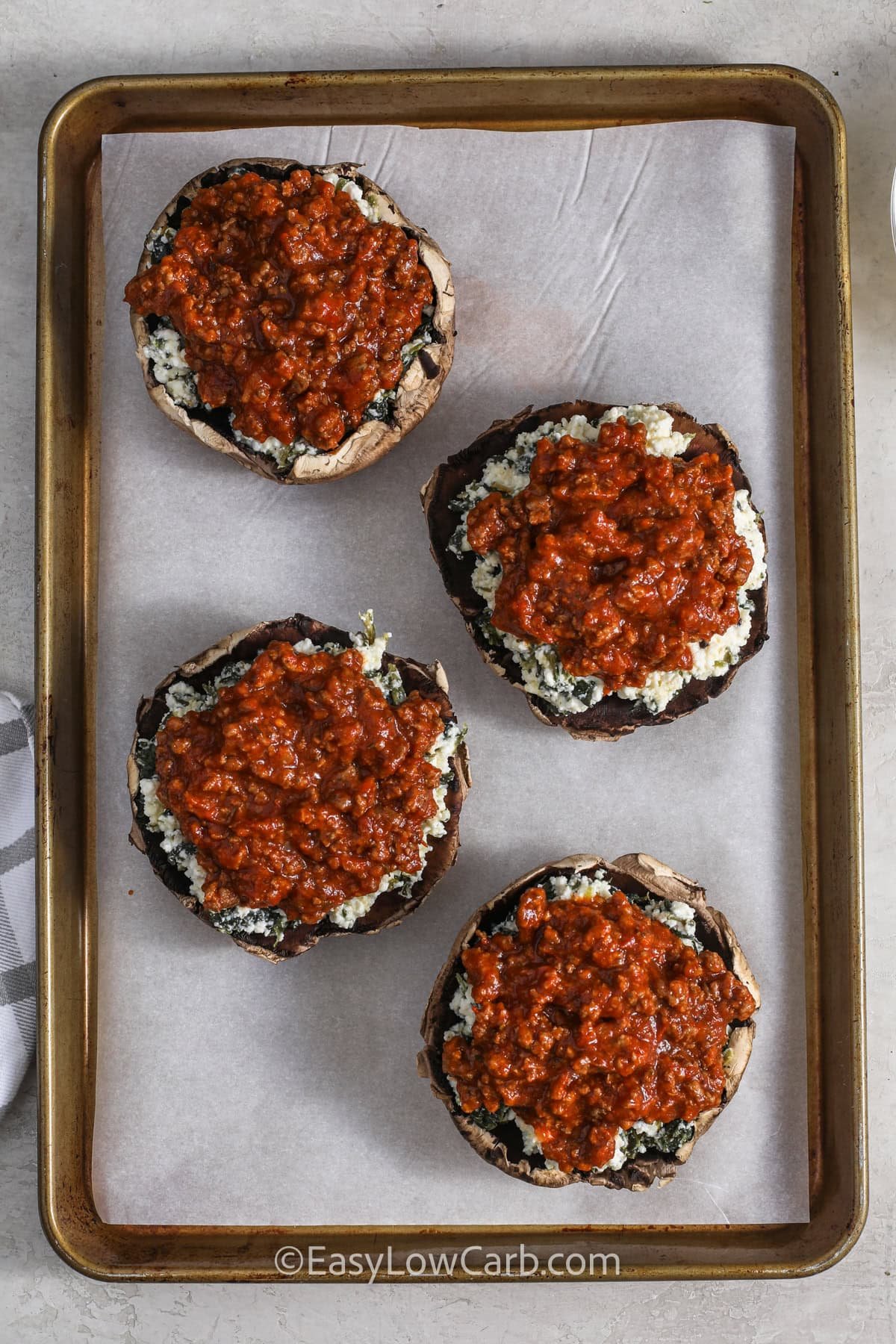 adding meat sauce to adding cheese to Lasagna Stuffed Mushrooms on a sheet pan before cooking