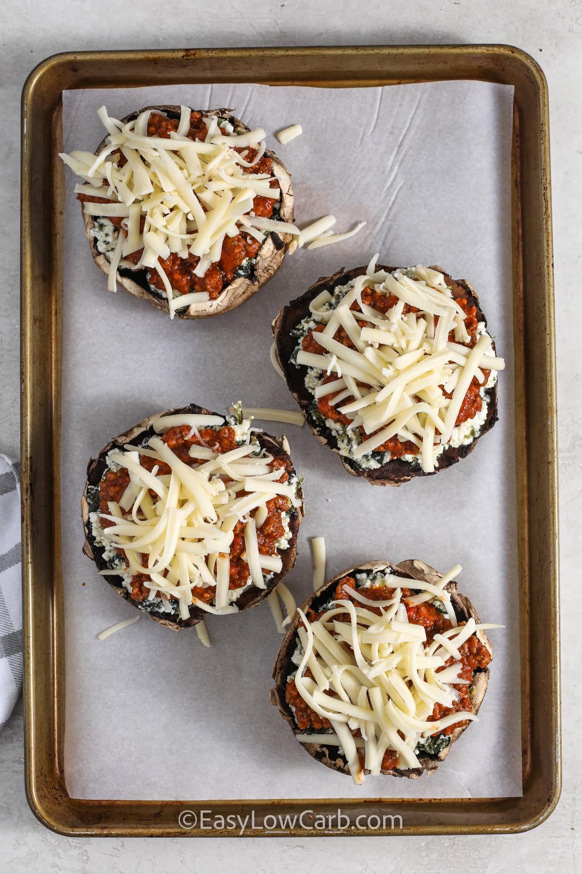 adding cheese to Lasagna Stuffed Mushrooms on a sheet pan before cooking
