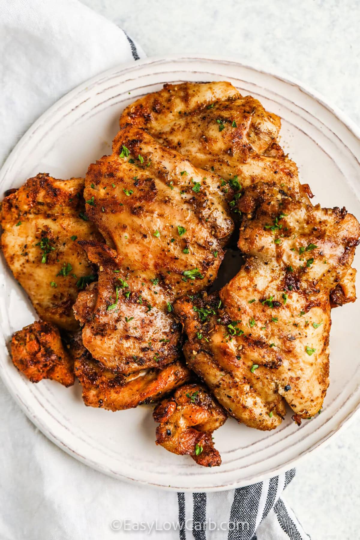 This grilled chicken thighs recipe is easy to make and creates a juicy and flavorful entree. A simple blend of olive oil, garlic powder, smoked paprika, and oregano adds the perfect seasoning. Let them marinate to soak in all the flavors, then grill until perfectly tender. Serve with fresh veggies or a crisp salad for a quick and satisfying meal that’s low-carb and delicious. Perfect for busy weeknights or meal prep. #easylowcarb Grilled Chicken Thighs on a plate