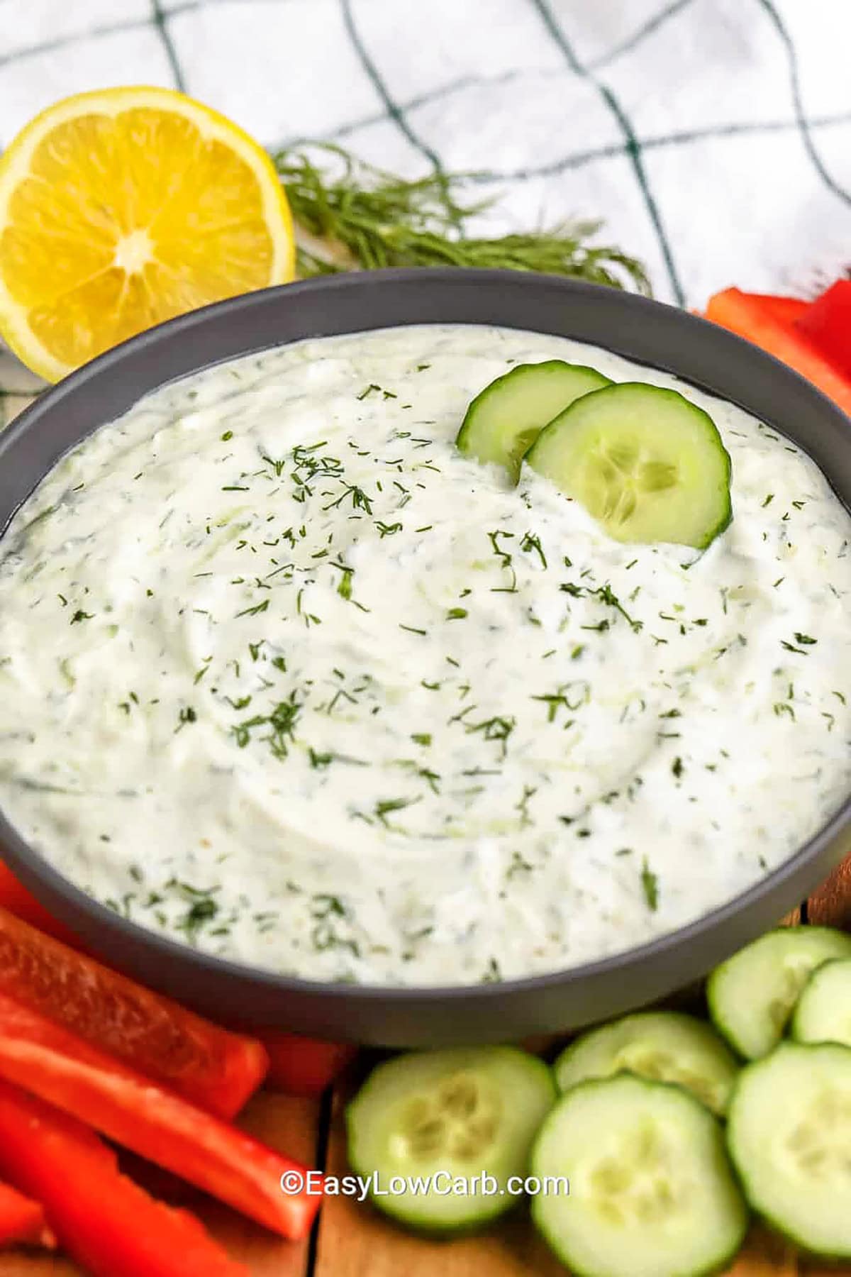 Homemade tzatziki is creamy, tangy, and packed with fresh flavors from grated cucumber, Greek yogurt, lemon juice, dill, and garlic. This easy dip is perfect for veggies, grilled meats, or as a refreshing spread. A touch of olive oil adds richness, while a pinch of salt brings out all the flavors. Simple to make and full of Mediterranean goodness, it's a must-have for any meal. #easylowcarb Homemade Tzatziki in a bowl with vegetables around the bowl