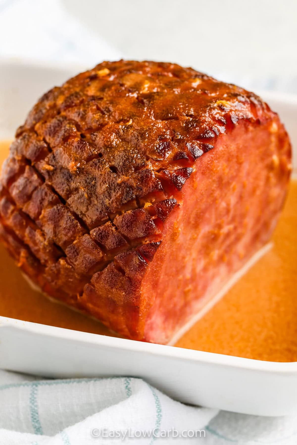 This low carb baked ham is a foolproof recipe that delivers big flavor with minimal effort. The sugar-free glaze caramelizes perfectly, creating a mouthwatering golden crust while keeping the ham juicy and flavorful. A mix of Swerve brown sugar, tangy Dijon mustard, and a hint of orange zest gives just the right balance of sweetness and zest. Baked low and slow, the ham stays incredibly tender and delicious. #easylowcarb juicy tender Low Carb Baked Ham in a dish